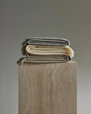 Stack of folded blankets on a wooden block against a gray background