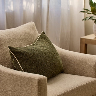 Beige armchair with a green pillow in a softly lit room.