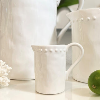 Set of white ceramic pitchers on a light surface with a green fruit and decorative item.